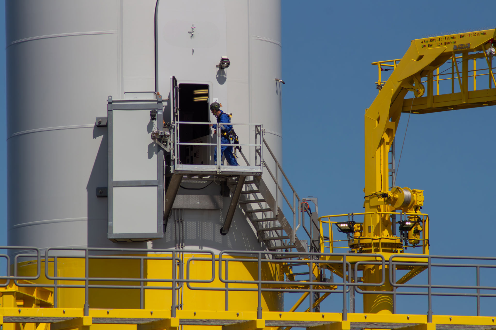 Wind turbine technician in safety harness entering the base of an offshore wind turbine tower